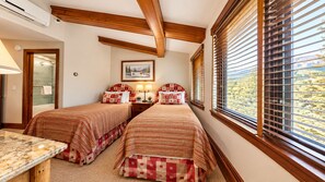Un dormitorio con dos camas, techo de madera, ventana con persianas y un cuadro en la pared.