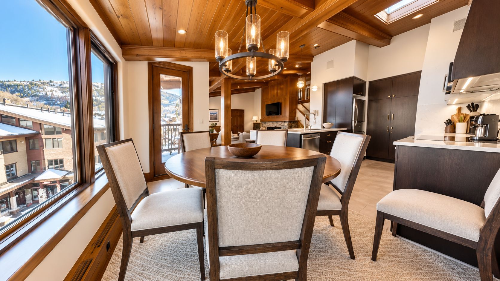 A modern kitchen with dark cabinetry, a central island, and a dining area with a round table and chairs.
