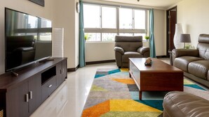 Uma sala de estar moderna com televisão de tela plana, sofás de couro, uma mesa de centro e um tapete colorido.