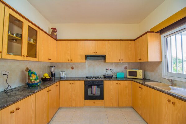 A kitchen with wooden cabinets, a stove, a microwave, and a sink. - Corallia Villa ,3 Bedrooms see and Forest View (Ayia Marina Chrysochous)
