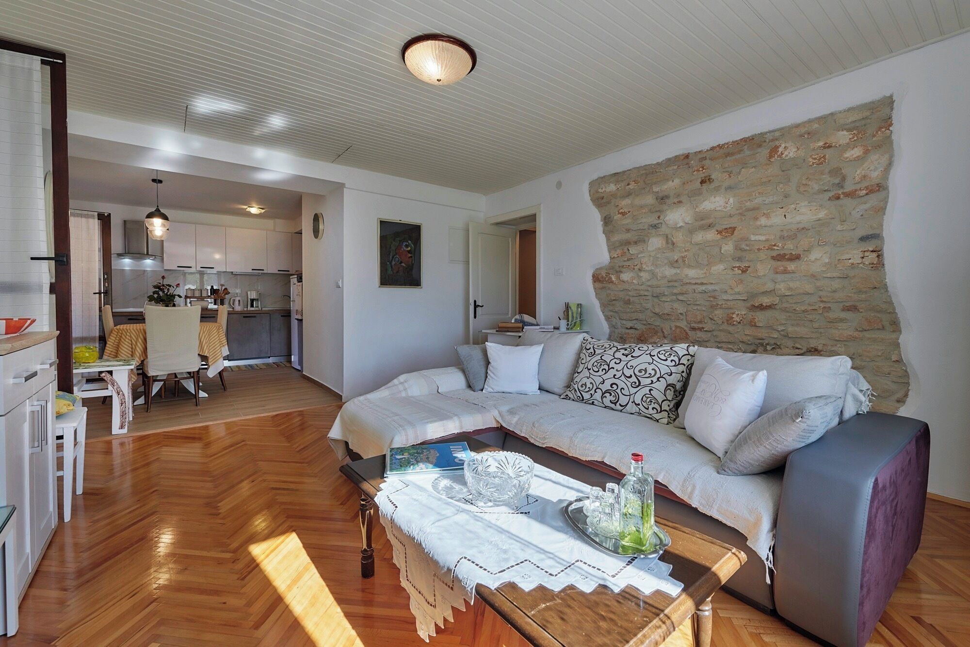 A modern living room with a wooden floor, a sofa set, a coffee table, and a kitchen in the background.