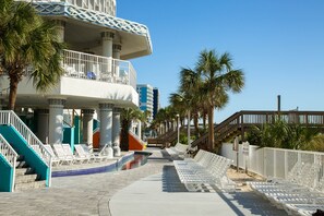 Un resort con piscina, sillas de descanso, palmeras y una escalera que lleva a un balcón.