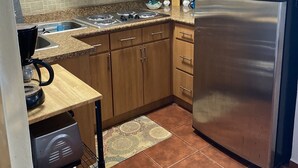 Een compacte keuken met houten kastjes, een roestvrijstalen koelkast, een magnetron en een gasfornuis.