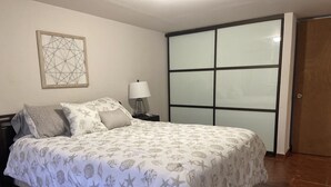 Een slaapkamer met een bed, nachtkastje, lamp, kunstwerk aan de muur en een schuifdeur.