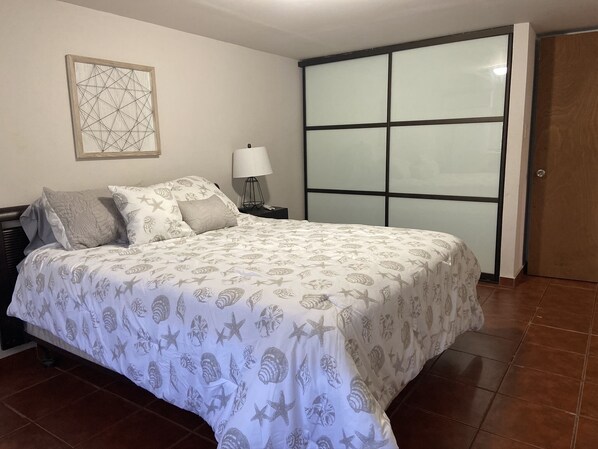 A bedroom with a bed, a nightstand, a lamp, a wall art piece, and a sliding door.