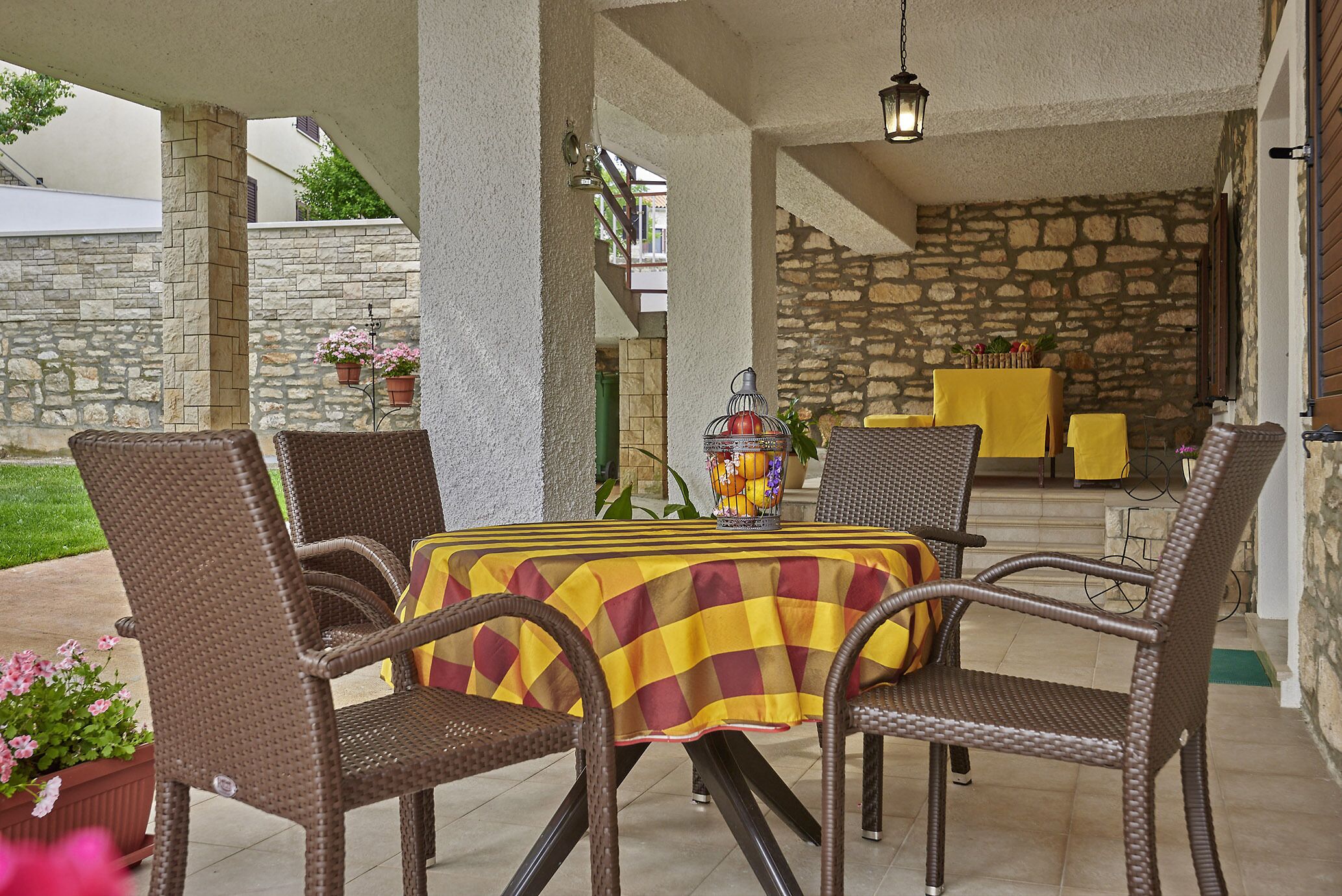Eine Terrasse im Freien mit Korbstühlen und einem Tisch, bedeckt mit einer karierten Tischdecke.