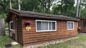 Una cabaña de madera con un porche pequeño, una ventana con persianas verticales y un buzón.