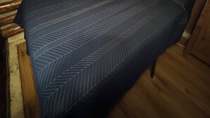 Una habitación con una cama frente a una pared de madera con troncos horizontales, suelo de madera y una ventana.