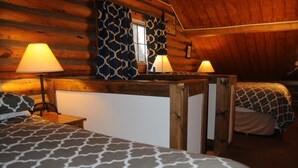 Ein gemütliches Blockhaus-Zimmer mit zwei Betten, einem Holztisch und zwei Lampen.