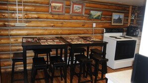 Ein rustikales Holzhaus-Interieur mit einem Holzespeisesaal, gedeckt für vier Personen, einem Herd und gerahmten Bildern an den Wänden.