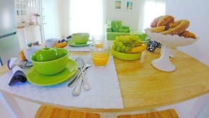 A breakfast table with green bowls, a glass of orange juice, a bowl of grapes, and a basket of croissants.