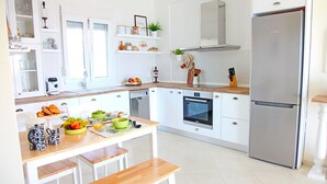 A modern kitchen with white cabinetry, a stainless steel refrigerator, a wooden dining table, and a bench.