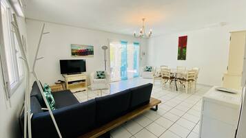Een woonkamer met een bank, televisie en een eethoek met stoelen en een tafel.