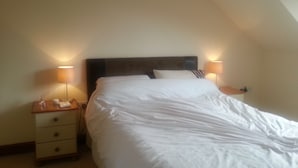 A neatly made bed in a room with a sloped ceiling, two bedside lamps, and a nightstand with a telephone and a tissue box. - Spacious  holiday cottage in Bowness on Windermere, Lake Distrct, Uk (Windermere)