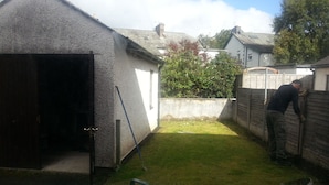 A residential backyard with a garage, a wooden fence, and a person working on the fence. - Spacious  holiday cottage in Bowness on Windermere, Lake Distrct, Uk (Windermere)