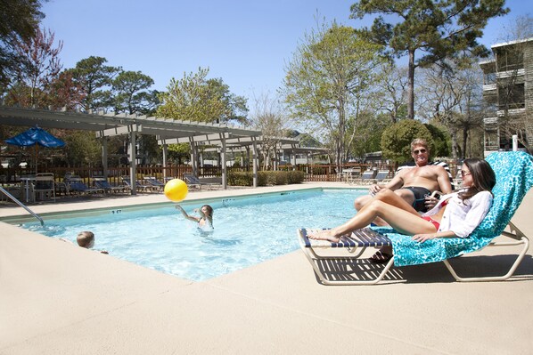 Zona de piscina con sillones reclinables, una pérgola y cielo despejado.