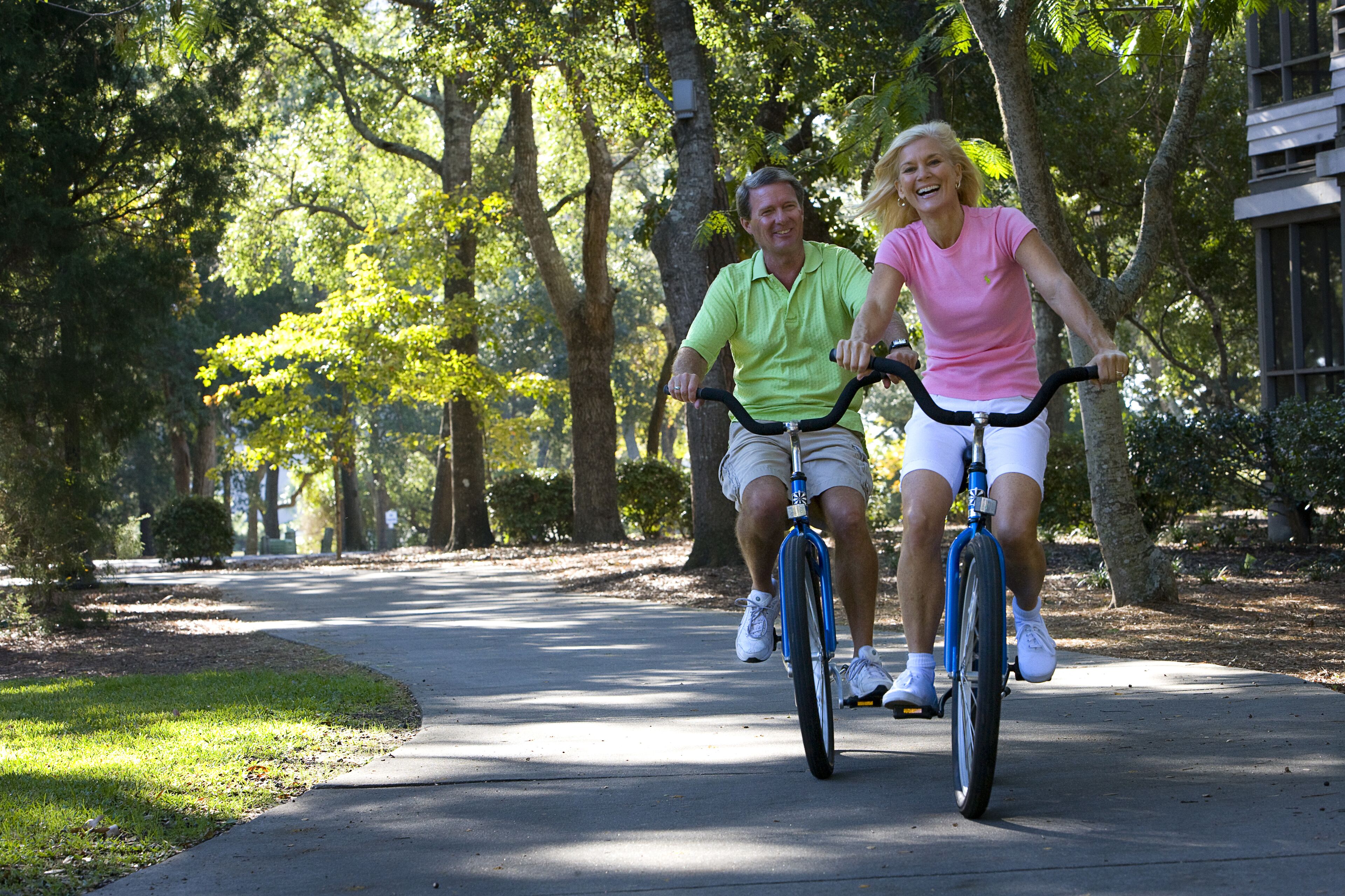 Two people riding bicycles on a tree-lined path.