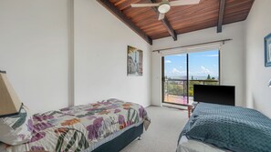 Ein Schlafzimmer mit Bett, Schreibtisch, Stuhl, Deckenventilator und einem Balkon mit Blick.