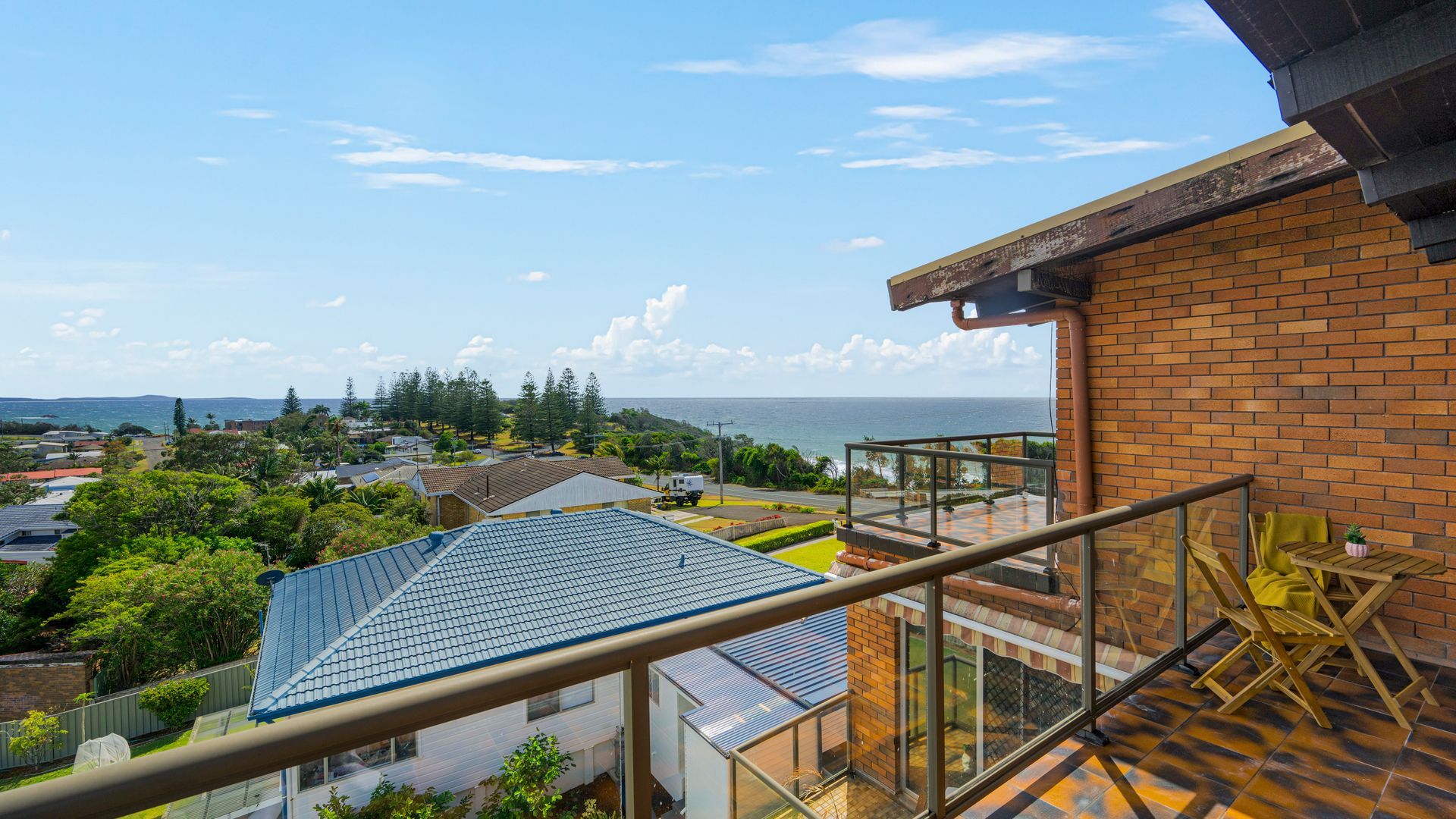Un balcón residencial con vista al mar, un muro de ladrillo y una barandilla de vidrio.