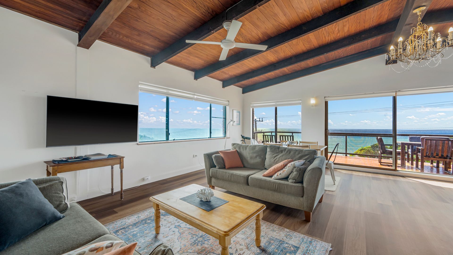 A spacious living room with a large window, a ceiling fan, and a view of the ocean.