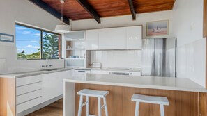 A modern kitchen with white cabinetry, a stainless steel refrigerator, and a large island with bar stools.