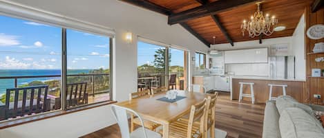 Un amplio espacio de sala con una gran mesa de madera, sillas blancas y vista al océano.