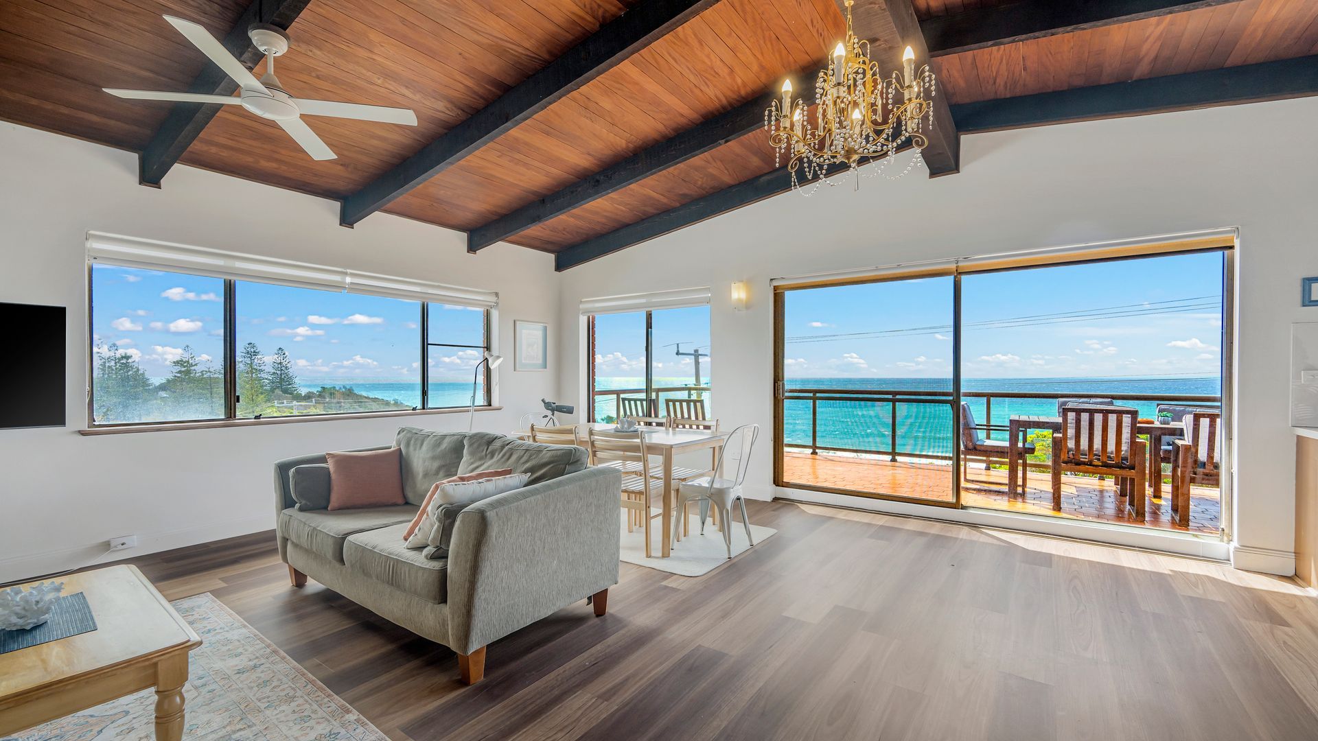 A spacious living area with a large window overlooking the ocean, a ceiling fan, and a chandelier.