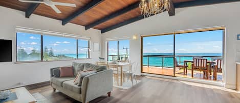 A spacious living area with a large window overlooking the ocean, a ceiling fan, and a chandelier.