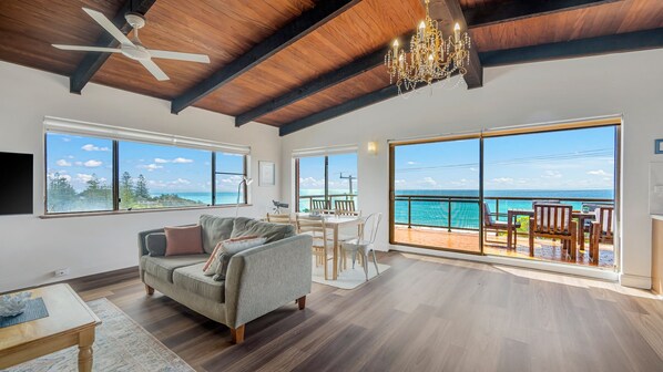 A spacious living area with a large window overlooking the ocean, a ceiling fan, and a chandelier.