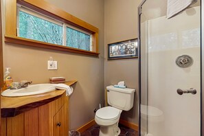 A bathroom with a wooden vanity, a toilet, a framed picture of dogs, and a glass shower enclosure. - Dog-friendly studio w/ kitchenette, WiFi, yard & fire pit (Orcas Island)