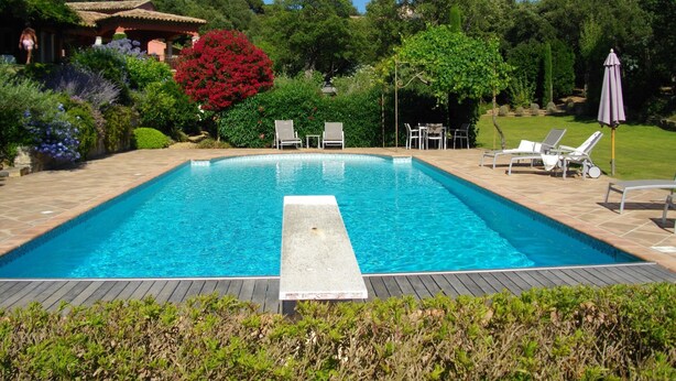 Una piscina rettangolare con un pontile in legno, circondata da vegetazione lussureggiante e un gazebo.