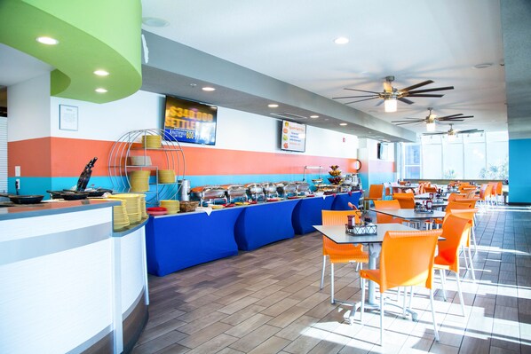 A buffet area with a counter, multiple food stations, and orange chairs.