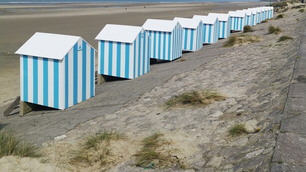 Una hilera de cabañas de playa con una vista despejada de la playa y el océano al fondo.