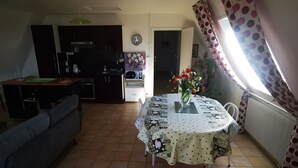 Una sala de estar con un sofá, una mesa de comedor con mantel floreado, y una cocina al fondo.