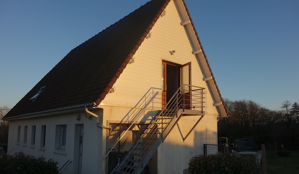 A white building with a steeply pitched roof, a small balcony with a metal railing, and a door leading to an interior space.