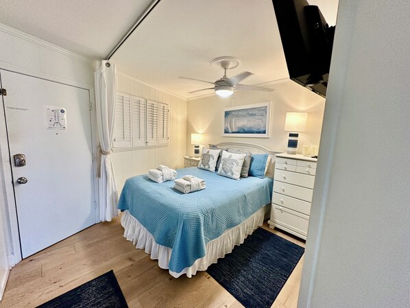 Ein Schlafzimmer mit einem Bett, Deckenventilator, Nachttisch, Kommode und einer Tür mit Schloss.