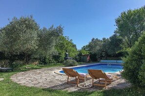 A swimming pool with two wooden lounge chairs and a stone pathway.