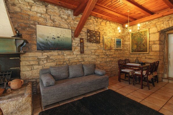 A cozy room with a stone wall, a gray sofa, a wooden dining table with chairs, and a chandelier.