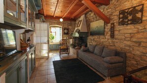 Un intérieur rustique avec un mur en pierre, des poutres en bois, une cheminée, un canapé et un coin repas comprenant une table et des chaises.