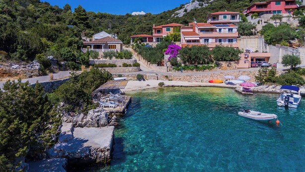 Un pueblo costero con aguas cristalinas, edificios de piedra y un muelle para embarcaciones.