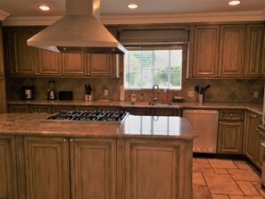 A kitchen with wooden cabinets, a central island with a stove, a window with blinds, and a sink. - Spacious luxury home in Sherman Oaks (Sherman Oaks)