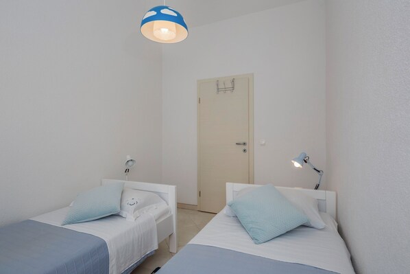 A small, clean room with two single beds, a door, and a hanging light fixture.