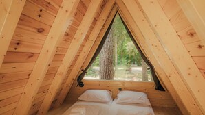 A wooden cabin with a triangular roof, two beds with white linens, and a window overlooking a forest. - Wooden hut 'Forest bed' near to the river Savinja (Mozirje)