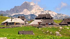 Un pueblo rural con casas de madera tradicionales, un muro de piedra y una montaña al fondo.