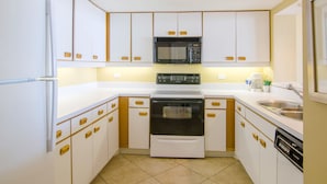 Una cocina compacta con armarios blancos, microondas, horno y lavavajillas.