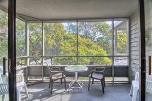 Enjoy a peaceful view of the tree-lined street from this sunroom with a large window, a round table, and two chairs.