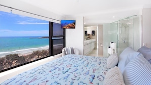 Un dormitorio con una cama grande, televisión, ducha de vidrio y vista al océano.