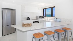 Una cocina moderna con una isla grande, electrodomésticos de acero inoxidable y vista al mar.