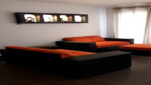 A living room with a black and orange sofa set, a flat-screen TV mounted on the wall, and a window with curtains. - CASTLEROCK SUITES AND CONDOS IN MEXICO CITY (México D.F.)