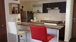 A compact kitchen with a central island, a refrigerator, and a microwave. There are two bar stools and a red chair. - CASTLEROCK SUITES AND CONDOS IN MEXICO CITY (México D.F.)